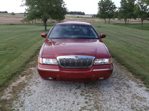 1999 Mercury Grand Marquis - A red Mercury Grand Marquis is parked on a gravel driveway with a rural landscape in the background.