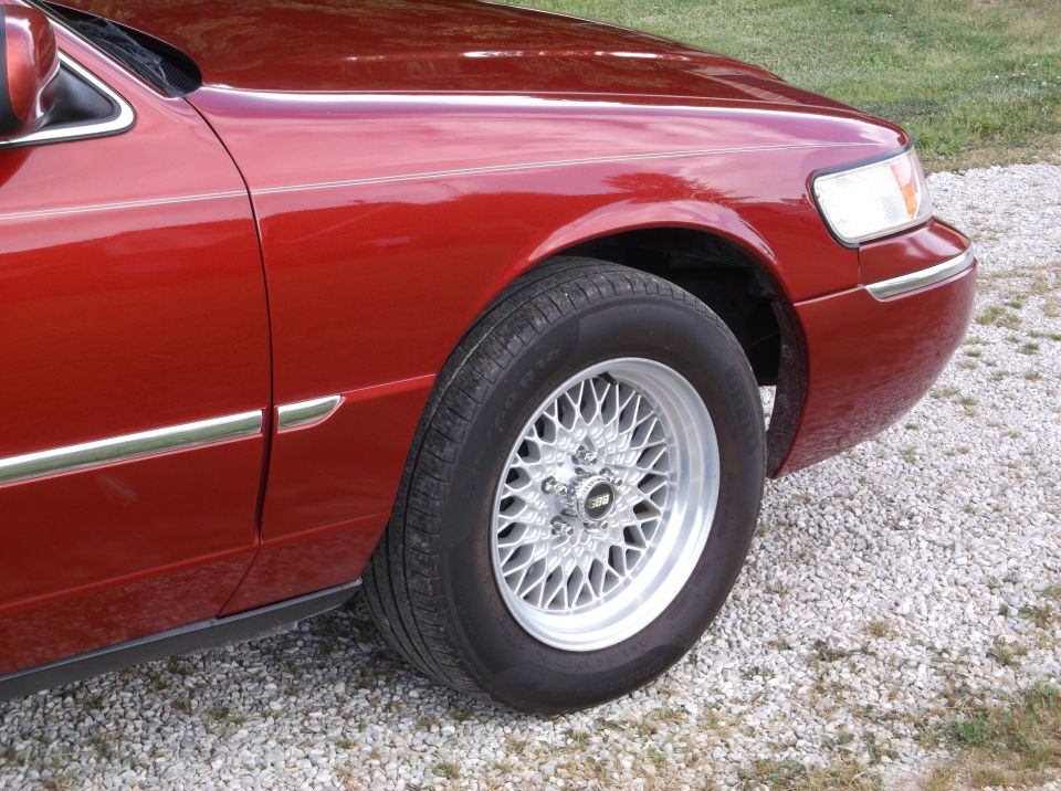 Red 1999 Mercury Grand Marquis with chrome trim and a mesh wheel