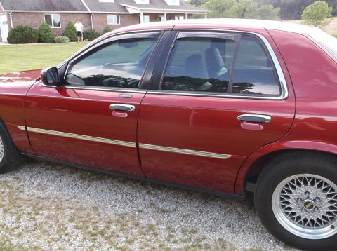 1999 Mercury Grand Marquis - Side profile of a red 1999 Mercury Grand Marquis sedan parked on a gravel driveway.