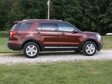 2016 Ford Explorer - A maroon 2016 Ford Explorer is shown from the side, parked on a gravel driveway with grass and trees in the background.