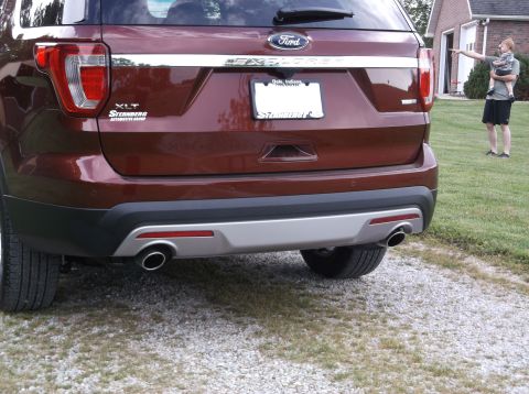 2016 Ford Explorer - The rear of a maroon Ford Explorer shows its taillights, chrome trim, and dual exhaust pipes.