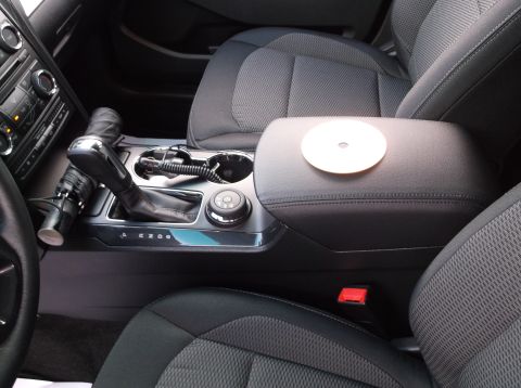 2016 Ford Explorer - The interior of a vehicle shows the center console area with a gear shifter and armrest. A white disc is placed on the armrest.