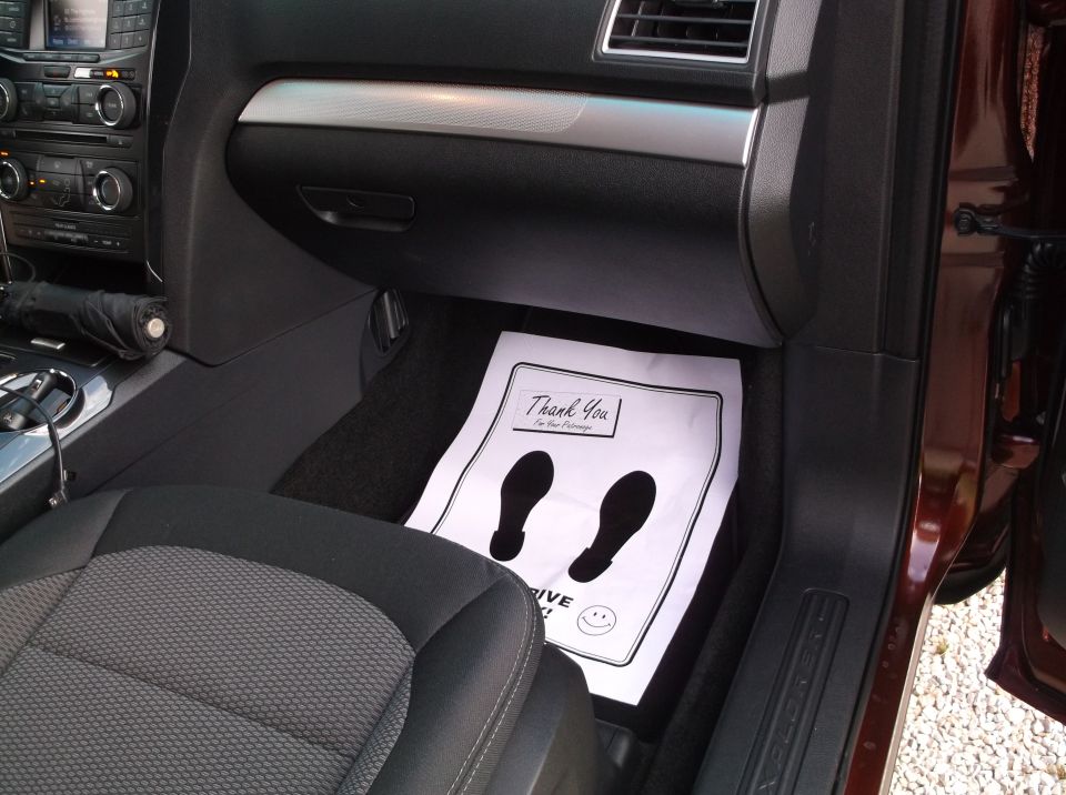 Dark interior of a car with a floor mat showing footprints and text, a seat, and dashboard controls