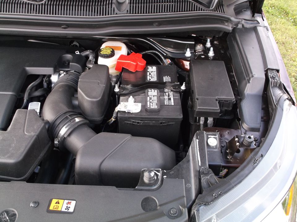 Engine bay with battery, air intake, and fuse box visible. The battery has text on it