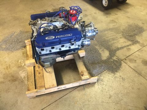 1982 Ford Bronco - A Ford Racing V8 engine sits on a wooden pallet, with gravel spilled on the floor around it.