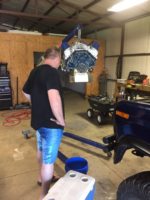 1982 Ford Bronco - A man observes an engine being lifted out of a vehicle in a garage setting.