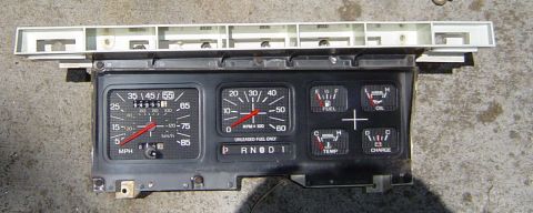 1986 Ford Bronco - A vehicle's instrument cluster, a speedometer, tachometer, and warning lights, is shown removed from its dash.