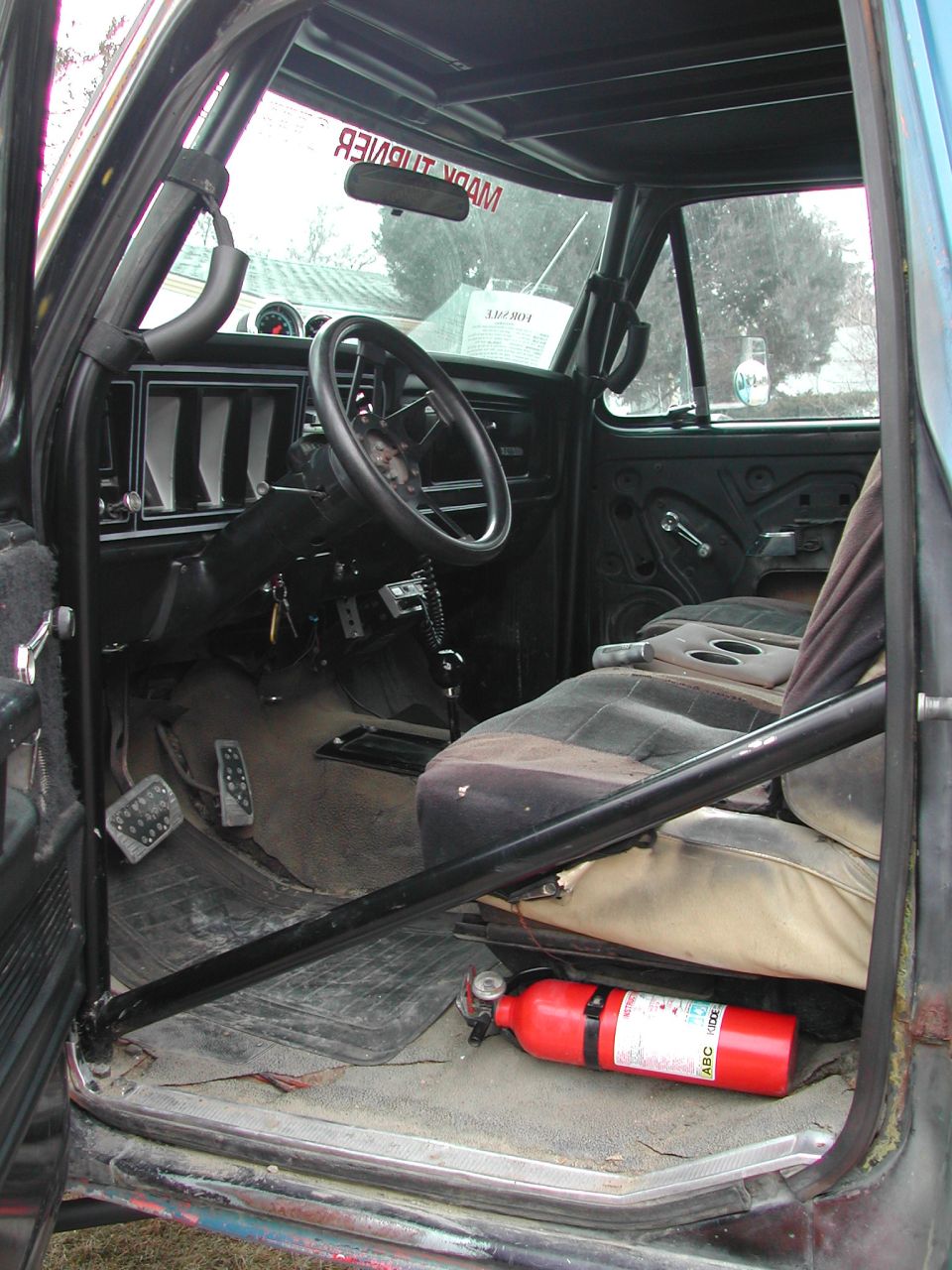 Stripped truck interior with roll cage, drilled pedals, bench seat and fire extinguisher on floor
