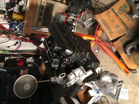 1987 Ford Bronco - A V8 engine is disassembled and staged on an engine stand amidst a cluttered garage environment.