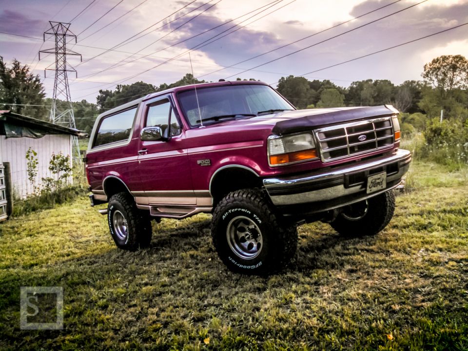 1996 Ford Bronco parked on grassy hill with power lines overhead