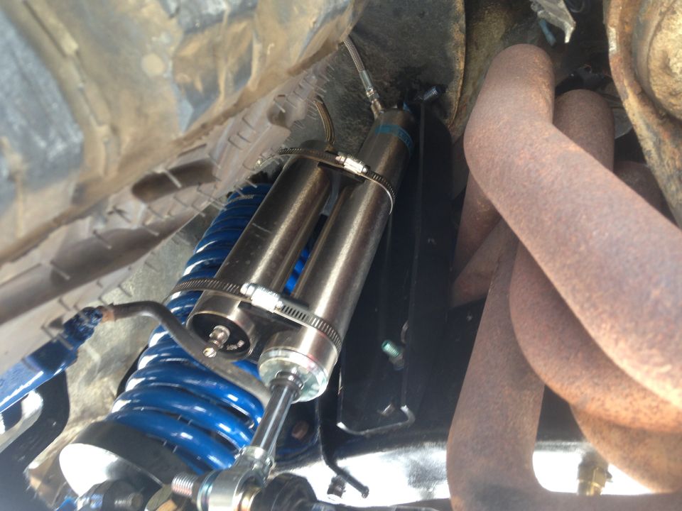 Close-up of a shock absorber and blue coil spring attached to rusty exhaust pipes