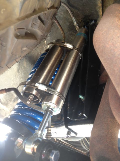 1979 Ford Bronco - Close-up view of aftermarket suspension components, including dual shock absorbers and blue coil springs, on a vehicle's underside.