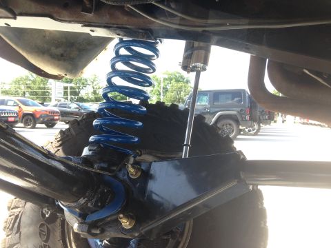 1979 Ford Bronco - Close-up view of a vehicle's blue coil suspension and shock absorber, with other vehicles visible in the background.