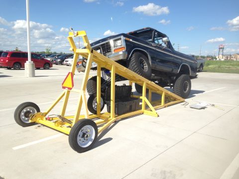 1979 Ford Bronco - Black Ford Bronco on a yellow trailer lift, lifted for suspension work. License plate visible.