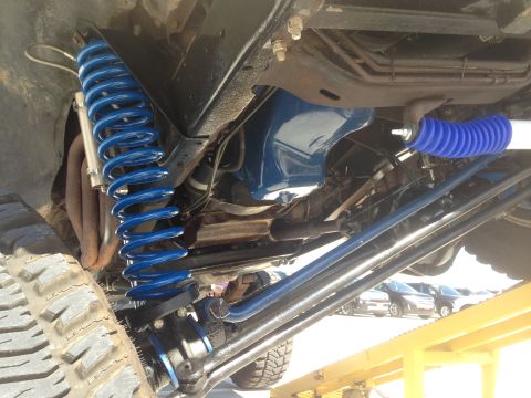 1979 Ford Bronco - The underside of a vehicle shows upgraded suspension parts, including bright blue coil springs and shock absorbers.