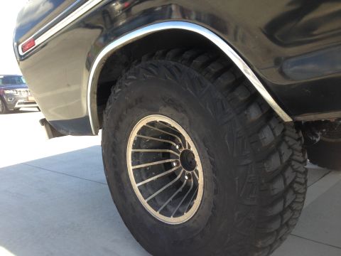 1979 Ford Bronco - A close-up shot focuses on the aggressive tread of a large tire and the chrome trim of a vehicle's fender.