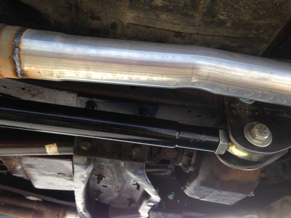 Undercarriage view of a vehicle showing a large diameter exhaust pipe, black suspension arm, and metal brackets