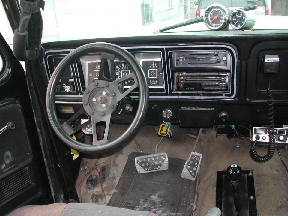 Truck dash with three-spoke wheel, aftermarket gauges, CB radio and stick shift on bare floor