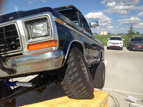 1979 Ford Bronco - A black 1979 Ford Bronco is shown with its suspension and large tires, with other vehicles in the background.