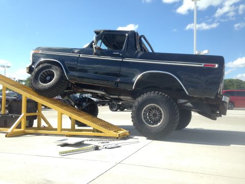 1979 Ford Bronco - Black Ford Bronco with lifted suspension is positioned on a yellow ramp outdoors.