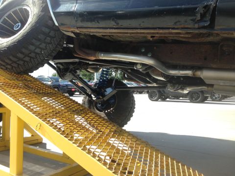 1979 Ford Bronco - The underside of a modified vehicle is shown on a ramp, with other cars visible in the background.