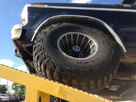 1979 Ford Bronco - Close-up of a black 1979 Ford Bronco's tire and fender, positioned on a yellow ramp.