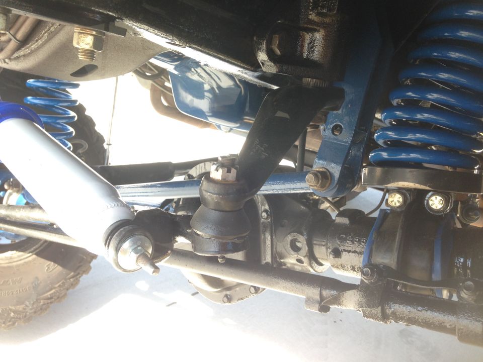 Close-up of a vehicle's front axle, steering linkage, and blue coil springs with a white shock absorber