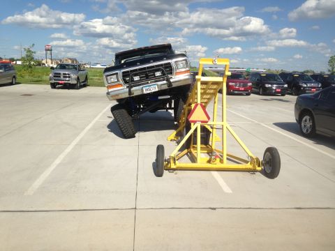 1979 Ford Bronco - A black 1979 Ford F-Series truck is elevated on a yellow lift in a parking lot.