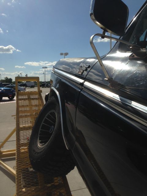 1979 Ford Bronco - A black Ford Bronco is positioned on a ramp, with another vehicle visible in the distance under a partly cloudy sky.
