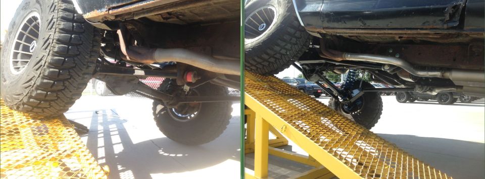 Underside view of two modified trucks on ramps. One has a lifted suspension and large tires