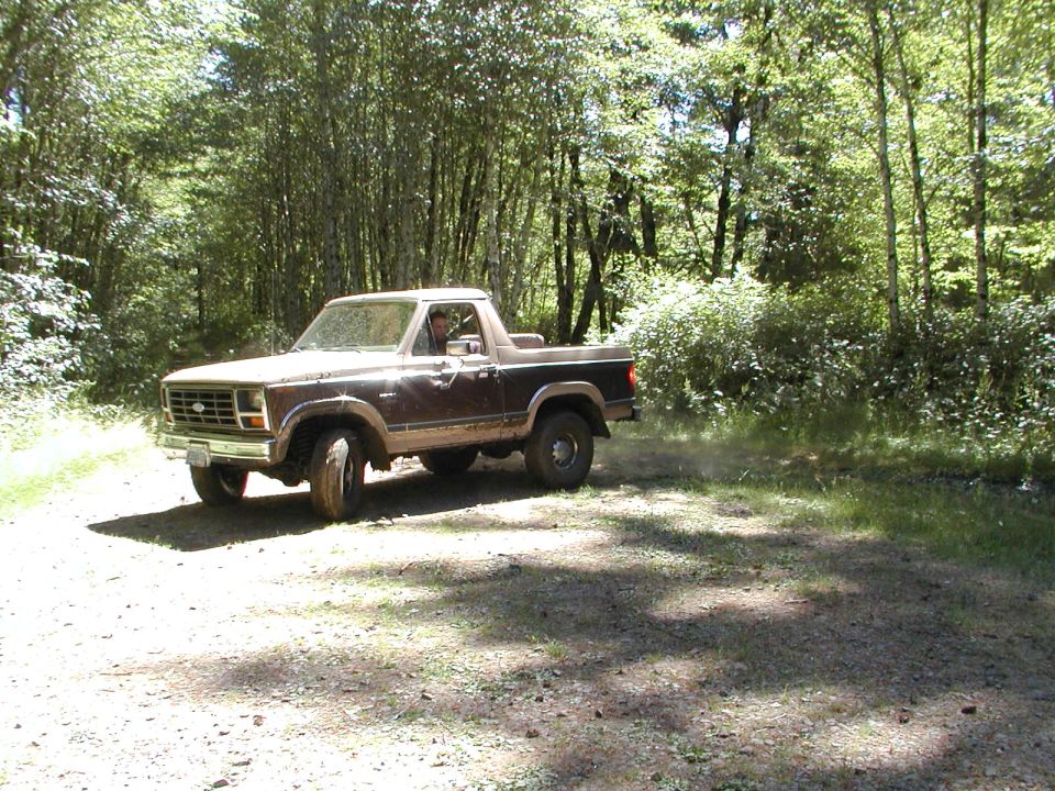 Brown 1980s Ford Bronco driving on a dirt road