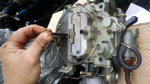 1978 Chevrolet C/K Pickup - Close-up of a carburetor with a hand adjusting a component. A hose is connected to the side.