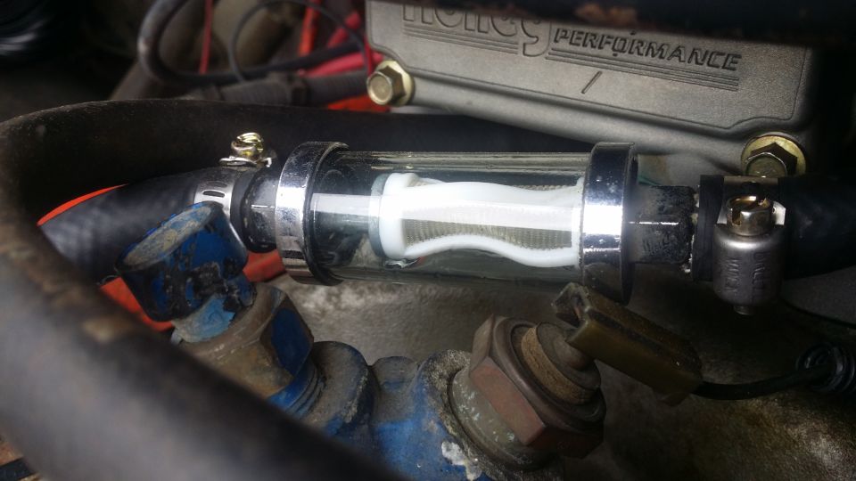 Chrome and glass inline fuel filter with white filter element, connected to black hoses