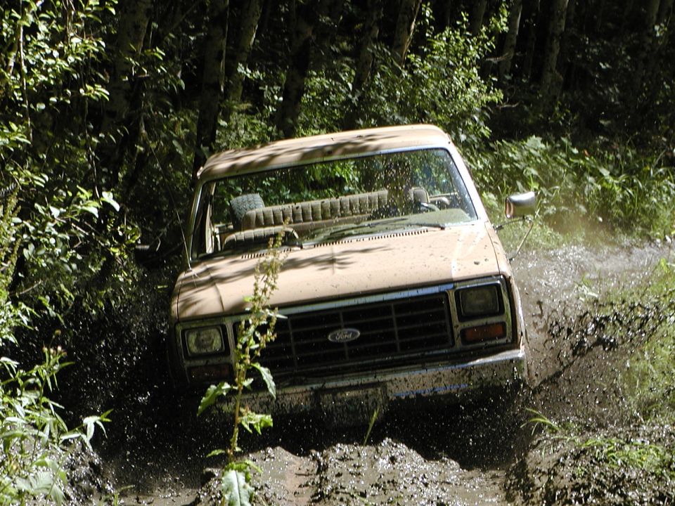 Tan Ford truck splashing through a muddy trail in the woods