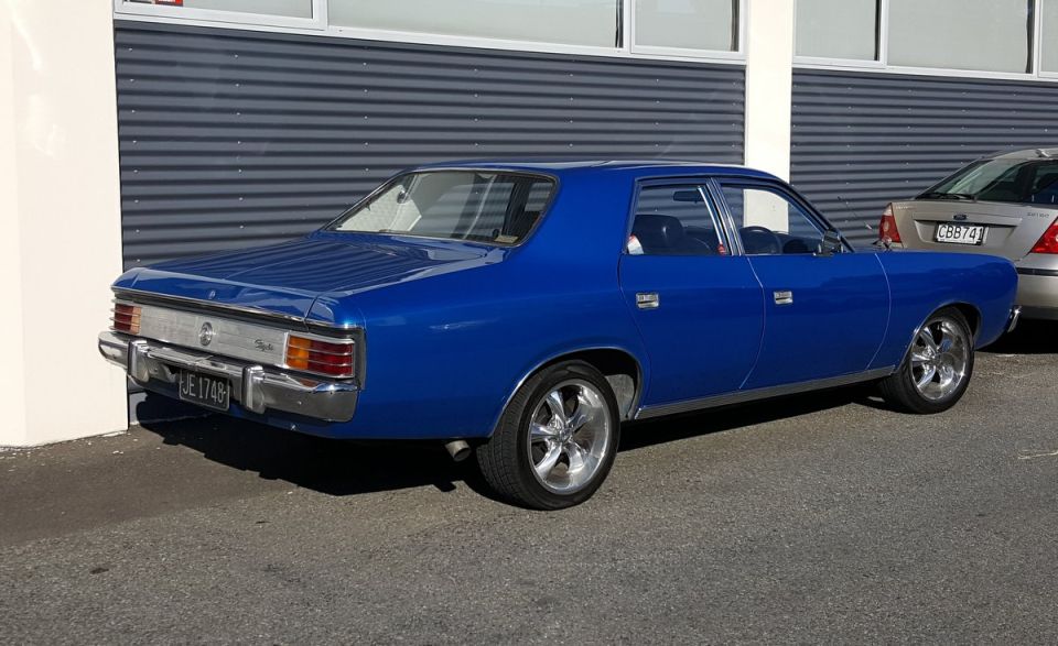 Blue sedan's rear 3/4 view with chrome wheels and a license plate reading JE 1748