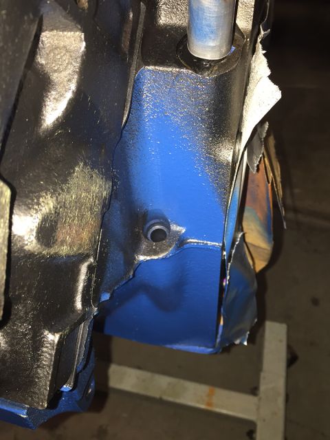 1978 Ford Bronco - Detail of an engine block, painted blue, with tape being removed from a surface.
