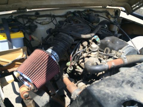 1987 Suzuki Samurai - The engine bay of a vehicle is shown, an aftermarket air filter and various engine parts.
