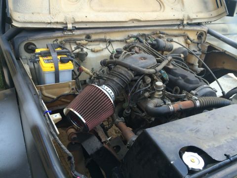 1987 Suzuki Samurai - The engine bay of a vehicle, an aftermarket air filter and a yellow Optima battery, is shown with the hood open.
