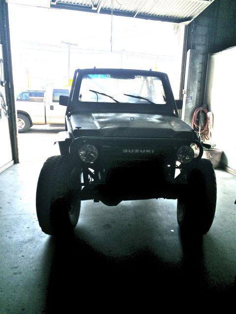 1987 Suzuki Samurai - A black 1987 Suzuki Samurai is parked head-on in a garage with large tires visible.