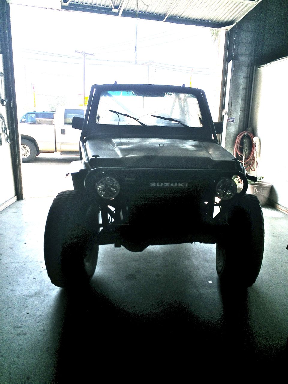 Black 1987 Suzuki Samurai with large tires, front view, parked indoors