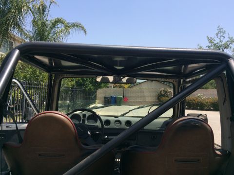 1987 Suzuki Samurai - The interior of a Suzuki Samurai shows brown seats and a roll cage, with a residential area visible through the windshield.