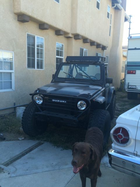 1987 Suzuki Samurai - Modified 1987 Suzuki Samurai in front of a building, with a dog and another vehicle nearby.