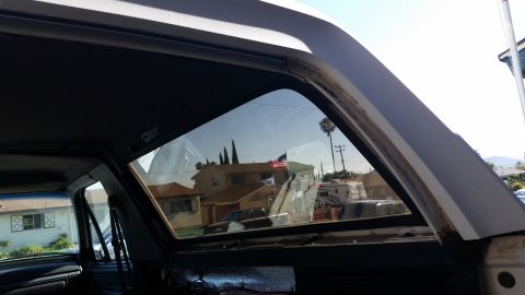 1992 Ford Bronco - View from inside a vehicle shows houses, trees, and an American flag reflected in the window.