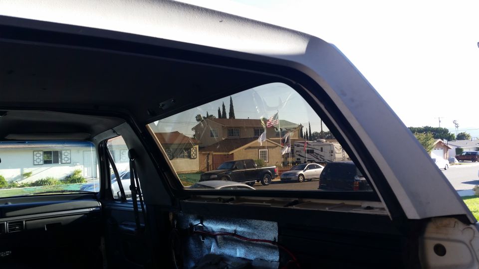 View from inside a vehicle looking out the side window at houses, a pickup truck, and a sedan