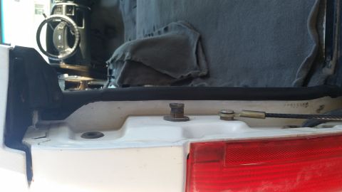 1992 Ford Bronco - Close-up of the rear interior trim and weatherstripping installation area in a white SUV. The steering wheel is visible in the background.