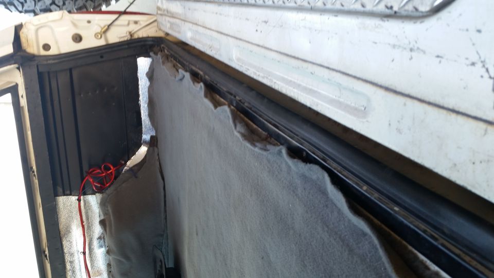 Interior view of a vehicle showing torn upholstery near the rear opening, with red wiring visible