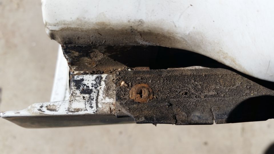 White automotive trim piece with rust and dirt, showing a screw head