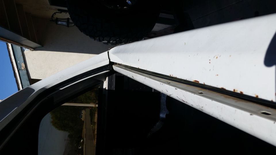 Close-up of white vehicle door frame showing rust spots and weatherstripping. Supermotors.net logo visible