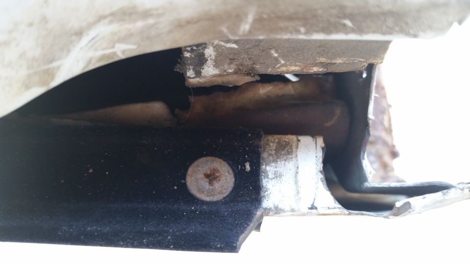Close-up of a rusty screw holding black trim to a white metal bracket on a vehicle's undercarriage