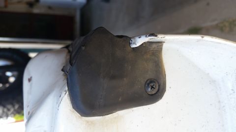 1992 Ford Bronco - A black rubber trim piece is secured to the white exterior of a vehicle with a screw.